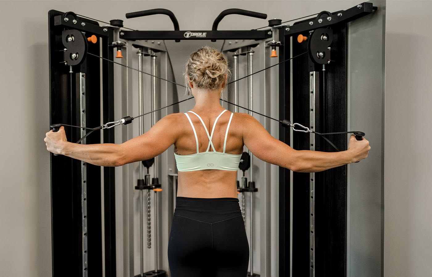A woman using a functional trainer to target her rear deltoids